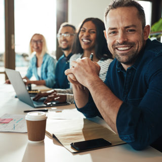 Smiling businessman sitting with a diverse group of coworkers during a meeting together at a table in an office