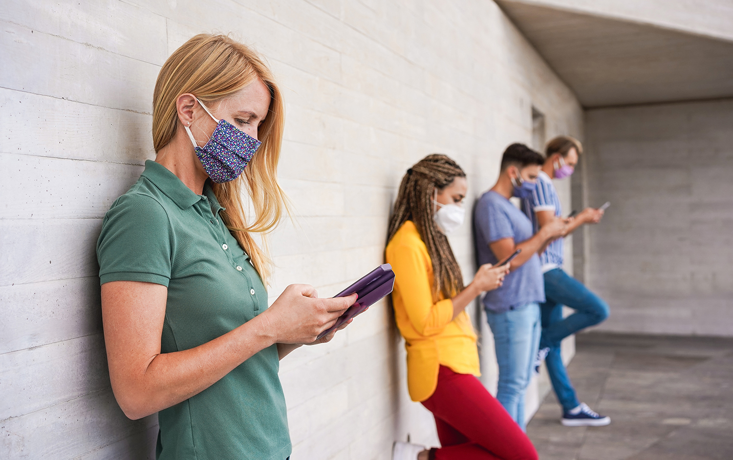 Young people wearing face safety masks using smart mobile phones while keeping social distance during coronavirus time - Technology and covid-19 spread prevention concept - Focus on blond girl hand