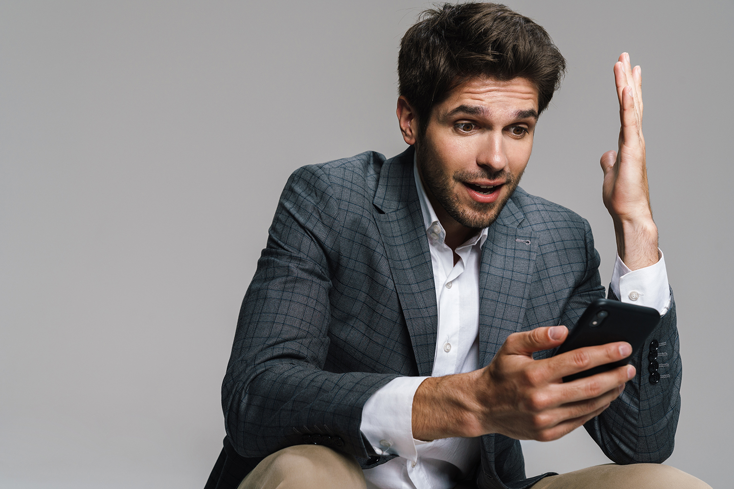 Photo of respectable surprised businessman using cellphone while siting isolated over grey wall